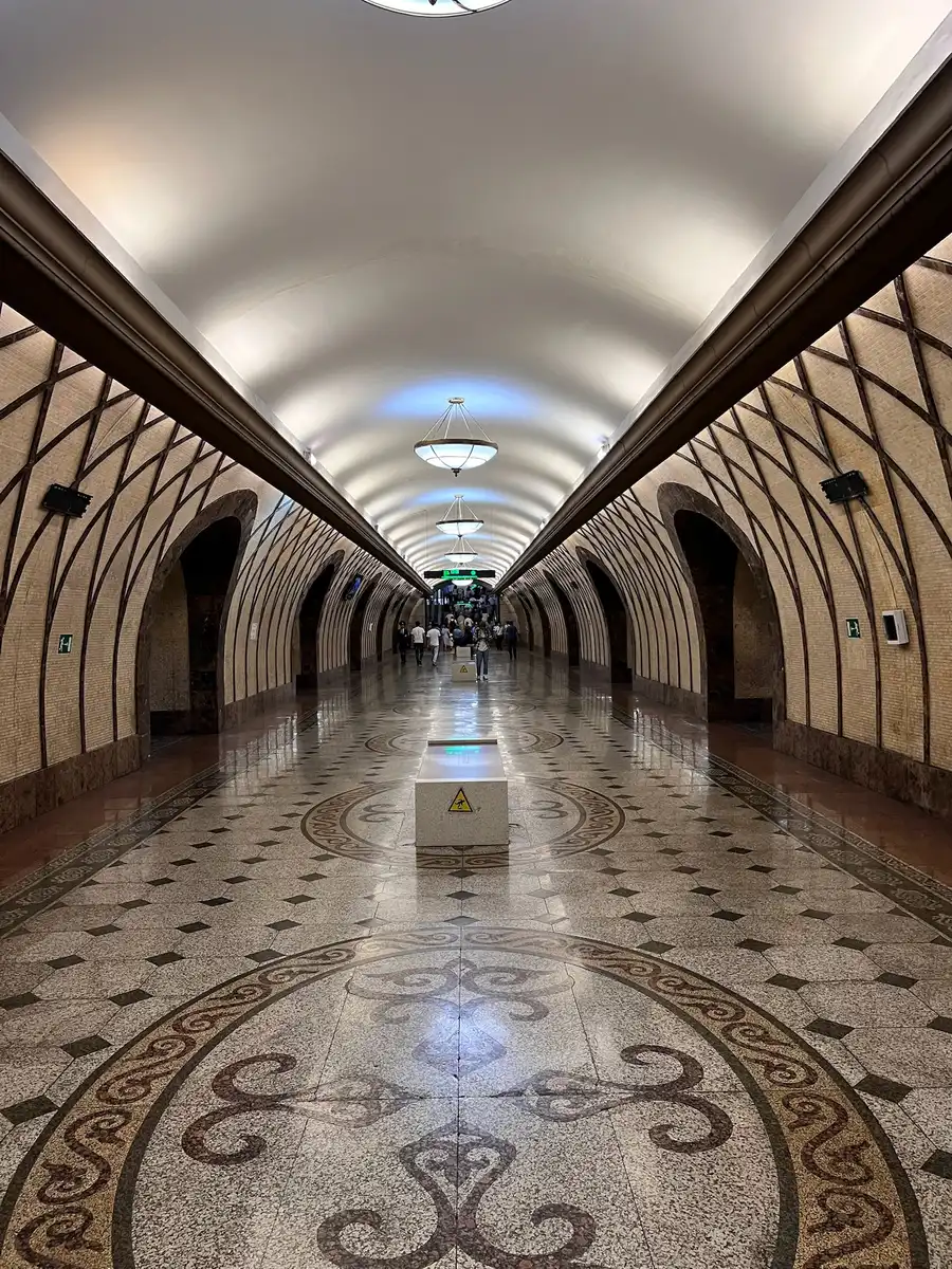 Ornately tiled underground platform of an Almaty metro station with decorative floor patterns and arched ceiling